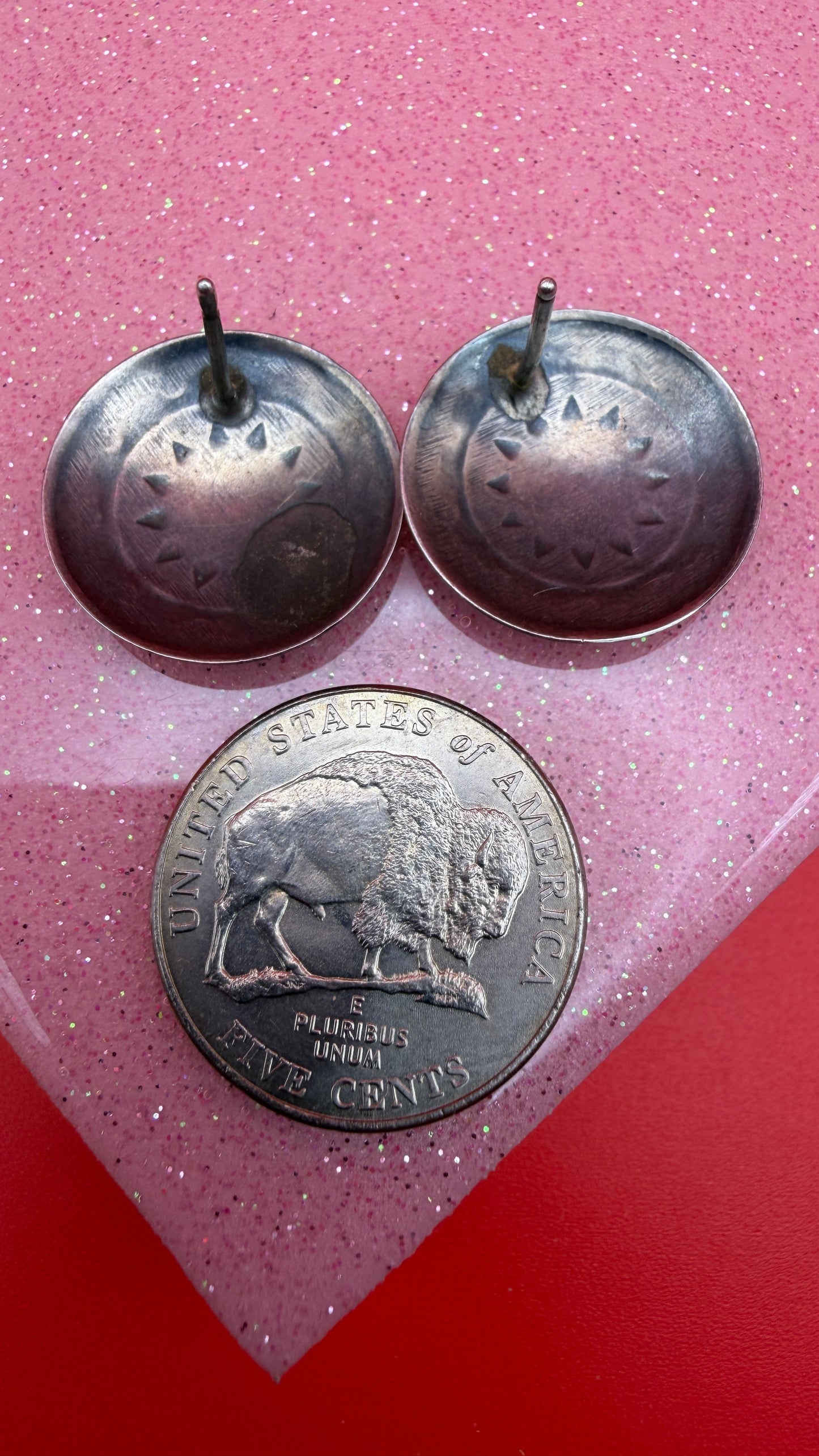 Two metal buttons with a coin featuring a buffalo design on a pink and red gradient background.