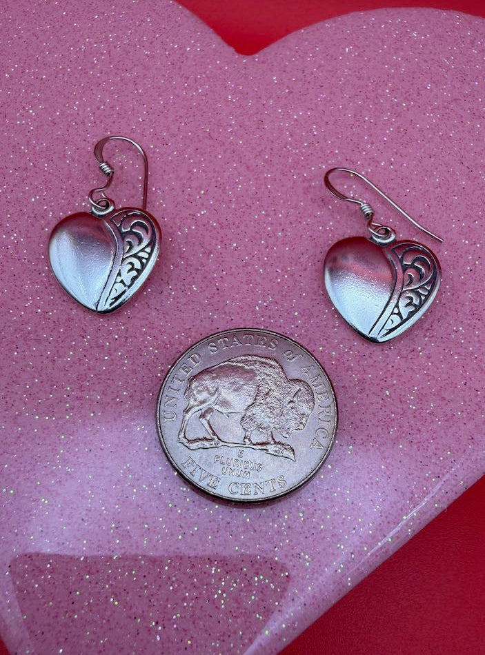 Silver heart-shaped earrings and a coin on a pink heart-shaped object with a red background